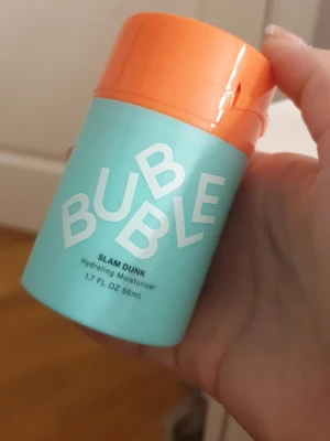 Bubble Slam Dunk Hydrating Moisturizer - Bubble Slam Dunk Hydrating Moisturizer i en snygg turkos och orange plastförpackning med pumpfunktion. Innehåller 50 ml återfuktande ansiktskräm som är vit och krämig i konsistensen. Perfekt för dig som vill ha en fräsch och enkel hudvårdsrutin.