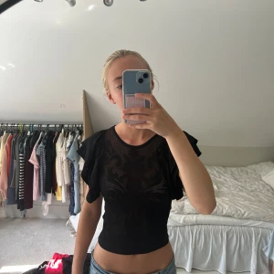 Svart croppad topp från Zara - Säljer en svart croppad topp från Zara med snyggt mönster framtill och volangärmar. Perfekt att styla med jeans eller kjol och funkar året om🌹🌹