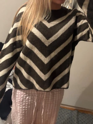 Brun och vit stickad tröja med zigzag - Säljer en brun och vit stickad tröja med coolt zigzag-mönster. Tröjan har långärmade och en loose passform som gör den superbekväm. Perfekt för att hålla sig varm under hösten och vintern. Snygg att styla med jeans eller mjukisbyxor.