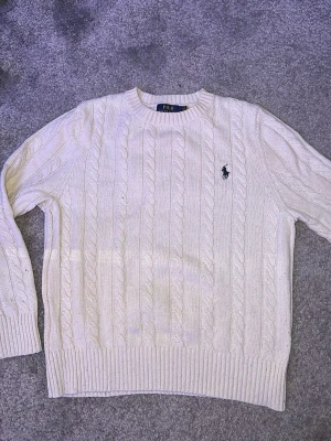 Vit kabelstickad tröja Polo Ralph Lauren - Vit kabelstickad tröja från Polo Ralph Lauren med klassisk rund hals och ribbade muddar. Tröjan har lång ärm och den ikoniska broderade loggan på bröstet. Perfekt för dig som gillar preppy stil och vill ha något som funkar hela året. Pris kan diskuteras 