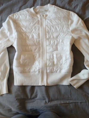 Vit quiltad jacka från Gina Tricot - Säljer en vit jacka från Gina Tricot med quiltad framsida och två fickor. Jackan har ribbade muddar, lång ärm och dragkedja framtill. Perfekt för dig som gillar stilrena och enkla plagg med lite extra struktur.