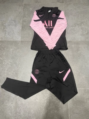 PSG x Nike tracksuit  - Säljer ett set med svarta och rosa PSG träningskläder från Nike, storlek S. Tröjan har halv dragkedja, rosa mönstrade ärmar och PSG-logga på bröstet. Byxorna är svarta med rosa detaljer och PSG-märke. Pris går att diskutera☺️