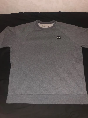 Grå sweatshirt från Under Armour - Säljer en grå sweatshirt från Under Armour i modellen ColdGear. Tröjan har en loose passform, rund hals och lång ärm. Materialet är mjukt och värmande, perfekt för kyliga dagar. Diskret logga på bröstet i svart och vitt. Enkel och stilren design.