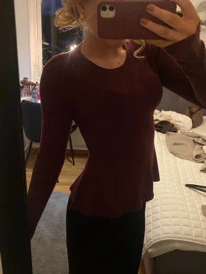 Mörkröd ribbad långärmad topp - Säljer en mörkröd långärmad topp med rund hals och lätt utsvängd nederdel. Toppen är ribbad och har en figurnära passform som framhäver midjan. Perfekt att styla med både jeans och kjol för en snygg look.