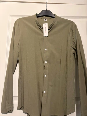 Olivgrön henley-skjorta med knappar - Nypris: 600kr / Olivgrön henley-skjorta från Onelife med lång ärm och vita knappar framtill. Skjortan har en enkel, stilren design med rund hals och är tillverkad i mjuk bomull som känns skön mot huden. Perfekt för dig som gillar minimalistisk stil.