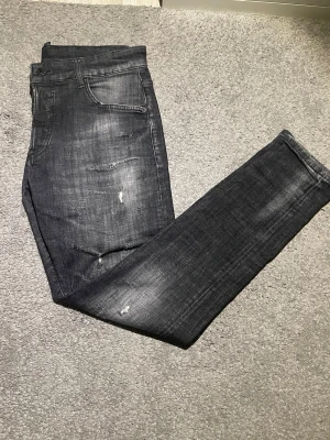 Svarta slim fit jeans från Dsquared2 - Säljer ett par svarta slim fit jeans från Dsquared2 med slitna detaljer och snygg tvätt. Jeansen har klassisk femficksdesign, låg midja och Dsquared2-lapp bak. Materialet är jeans med stretch för skön passform. Perfekt för dig som gillar streetstyle.
