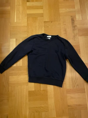 Mörkblå sweatshirt från Grunt - Säljer en stilren mörkblå sweatshirt från Grunt i storlek M I BARN STORLEK. Tröjan har rund hals, ribbade muddar och ett diskret G-logotyp på bröstet. Tillverkad i mjuk ekologisk bomull som känns skön mot huden. Perfekt för chill dagar och enkel att matcha med jeans.