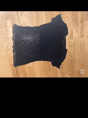 Svart mesh blus med volangdetaljer - Säljer en svart blus i mesh med volangdetaljer vid ärmslut och nederkant. Toppen har en genomskinlig, mönstrad mesh nedtill och på ärmarna. Ingen strl står men gissar på Xs eller S. Perfekt nu till nyår eller annat!!