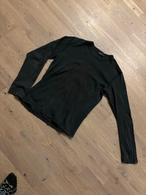 Svart långärmad topp från Mexx - En enkel och stilren svart långärmad topp från Mexx i storlek M. Toppen har rund halsringning med ribbad kant och är gjord i mjukt bomullsmaterial. Perfekt att matcha med jeans eller kjol för en clean look.