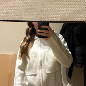 Vit stickad kofta med dragkedja - Säljer en stilren vit stickad kofta från åhlens i storlek XS. Koftan har två stora fickor framtill, krage och hel dragkedja. Materialet är mjukt och har en lätt struktur, perfekt för lager-på-lager. Passformen är normal och ärmarna är långa. Helt ny!