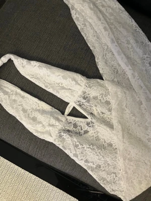 Vit lång jumpsuit med lace - Säljer en vit långklänning i spets med omlott och knyt i nacken. Klänningen är ärmlös och har ett snyggt spetsmönster över hela plagget. Perfekt för dig som gillar romantisk och feminin stil. Passar till sommarens alla tillfällen.