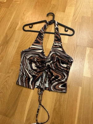 Brun och svart mönstrad topp - Säljer en snygg topp med abstrakt mönster i brunt, svart och vitt. Toppen har snörning framtill som ger en cool rynkad effekt och croppad passform. Materialet är mjukt och stretchigt, perfekt för att styla med jeans eller kjol eller till fest.