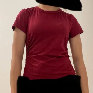 Vinröd t-shirt med snörning i sidan (FRI FRAKT TILL 5/1)‼️ - Snygg vinröd t-shirt med korta ärmar och rund hals. T-shirten har en cool snörningsdetalj längs ena sidan som ger en unik look. Materialet känns mjukt och stretchigt, perfekt för dig som gillar bekväma och stilrena plagg.