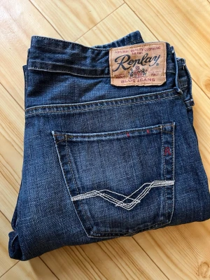 Replay Jennon blå jeans straight fit - Snygga blå jeans från Replay, modell Jennon, med klassisk femficksdesign och raka ben. Jeansen har kontrastsömmar, Replay-logga på bakfickan och detaljer i rött. Tillverkade i slitstarkt denimtyg av bomull. Perfekt för dig som gillar en tidlös och clean look.