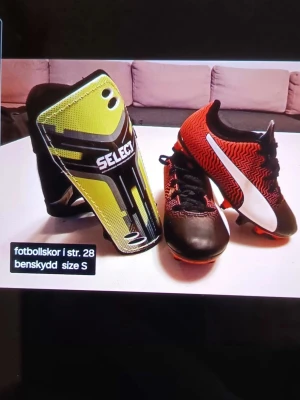 Svarta och röda fotbollsskor strl 28 - Säljer ett par fotbollsskor från Puma i storlek 28. Skorna har en snygg kombination av svart och röd färg med vit detalj på sidan och mönstrad ovandel. Utrustade med snörning och dobbar för bra grepp på planen. Perfekt för unga fotbollsspelare.