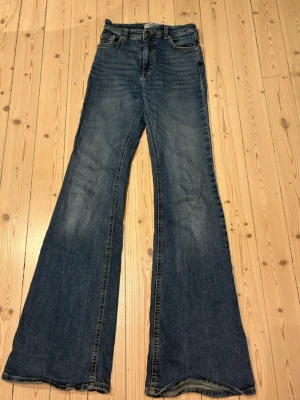 Högmidjade Bootcut jeans i mörkblå denim - Säljer ett par klassiska bootcut jeans från Pull&Bear i mörkblå denim. Byxorna har fem fickor, knapp och dragkedja. Passformen är normal och materialet är robust jeans. Perfekt för dig som gillar stockholmstil men inte vill visa hela magen 