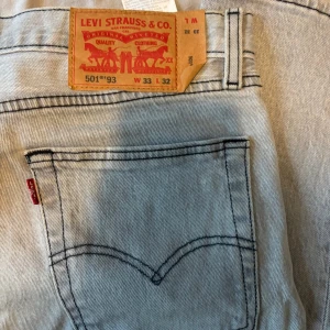 Levi's 501 ljusgrå jeans W33 L32 - Säljer ett par klassiska Levi's 501 jeans i ljusgrå tvätt. De har raka ben, fem fickor och tydliga svarta sömmar. Jeansen är tillverkade i bomull och har den ikoniska röda Levi's-taggen på bakfickan.
