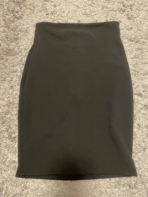 Svart figurnära kjol med hög midja - Stilren svart figurnära kjol med hög midja. Enkel och slät framtill för en snygg, minimalistisk look, med diskret söm baktill som ger fin passform och form. Tidlös modell som är lätt att matcha – perfekt både till vardag och fest. Den är i storlek petite xs och köpte den för inte så länge sedan. Säljer den i anledning av att den inte passar🖤