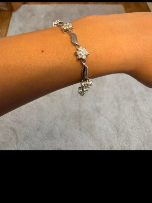 Ingen väst på bilderna - Bilderna visar ett armband i silverfärg med blommiga detaljer, men ingen väst finns med.