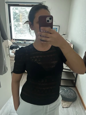 Svart spetsblus från Vila - Säljer en svart blus från Vila i storlek M. Blusen är helt i spets med korta ärmar och rund halsringning. Den har ett genombrutet mönster som ger en snygg och trendig look. Perfekt att styla med jeans eller kjol för en cool outfit.