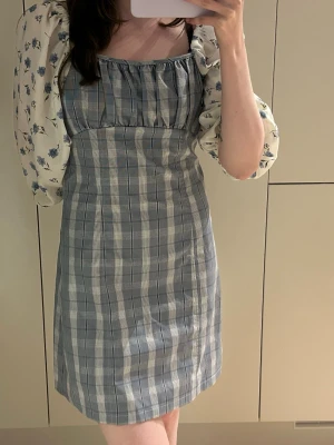 Klänning i pläd med smockad topp och blommiga ärmar - Sister Jane - Otroligt vacker klänning från Sister Jane som skulle passa till dem flesta tillställningar men även som vardagsplagg. Mönstret i pläd har inslag av glitter. Ärmarna har insydda elastiska band både upptill och nedtill, den kan därför bäras som square neck, eller off shoulder  Storlek S, visas på mig som är 160cm lång   Klänningen kommer tyvärr inte till användning för mig då den är lite stor💕