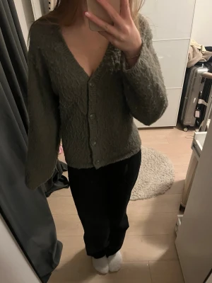Grön kofta med v-ringning och knappar - Mysig grön kofta med v-ringad hals och fyra matchande knappar framtill. Koftan har långärmade, lite loose ärmar och är tillverkad i ett stickat material som ger en fluffig känsla. 