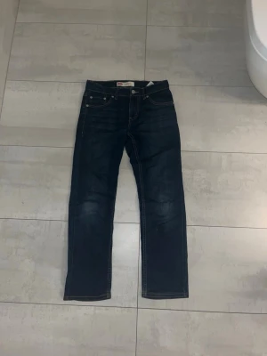 Levi's 511 mörkblå jeans - Snygga Levi's 511 jeans i mörkblå tvätt med klassiska fem fickor och kontrastsömmar. Modellen har en slim passform och raka ben, perfekt för dig som gillar en modern stil. Tillverkade i slitstarkt jeansmaterial med knapp och dragkedja framtill.