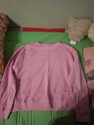 Ljusrosa sweatshirt med guldknappar - En ljusrosa sweatshirt med rund hals och långa ärmar. Tröjan har snygga guldknappar på ena axeln som extra detalj. Perfekt för dig som gillar en enkel men ändå unik stil. Tillverkad i mjukt bomullsmaterial för skön känsla.