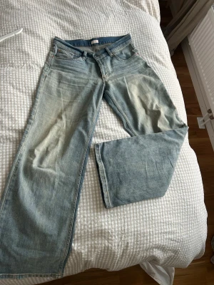 Wide jeans från Nelly i ljusblå denim - Säljer ett par ljusblå jeans från Nelly med breda ben och klassisk femficksdesign. Jeansen har normal passform och är tillverkade i jeansmaterial med snygga slitningar framtill. Perfekt för dig som gillar en avslappnad och trendig look.