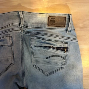 Ljusblå straight jeans från G-Star RAW - Säljer ett par ljusblå straight jeans från trendiga G-Star RAW med dragkedjedetalj på bakfickan och med otroligt passform. Jeansen har låg midja och slits