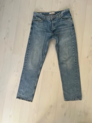 Loose fit jeans från Jack & Jones - Snygga ljusblå jeans från Jack & Jones i modellen Loose/Chris. De har en loose passform, raka ben och klassisk femficksdesign. Materialet är jeans i bomull och midjan är normal. Perfekt för dig som gillar avslappnad stil. Lite slitna på baksidan men det är lagat, se bild 4.