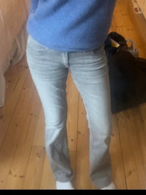 Ljusgrå bootcut jeans - Säljer ett par ljusgrå jeans med bootcut-snitt. Jeansen har klassisk femficksdesign och är tillverkade i mjukt denim-material. Passformen är normal och midjan är midwaist. Perfekta för dig som gillar en avslappnad och stilren look.
