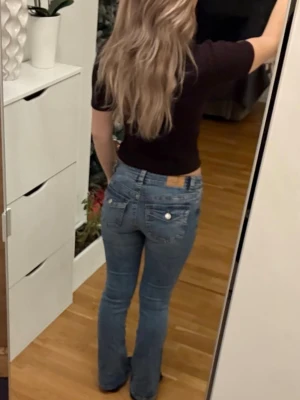 Blå bootcut jeans från Gina Tricot - Säljer ett par ljusblå bootcut jeans från Gina Tricot med klassisk femficksdesign och snygga knappar på bakfickorna. Jeansen har normal passform och är lowwaist. Tyvärr sitter dom för tight på mig skulle behålla dom annars.