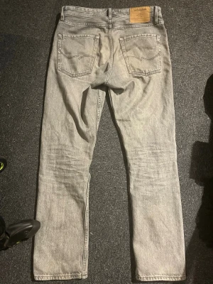 Grå jeans från Jack & Jones, relaxed chris - Säljer ett par ljusgrå jeans från Jack & Jones med klassisk femficksdesign och raka ben. Storlek 28/30, Modell relaxed chris. Jeansen har en snygg tvättad look och är tillverkade i slitstarkt bomullsmaterial. Perfekta för dig som gillar en enkel och clean stil.