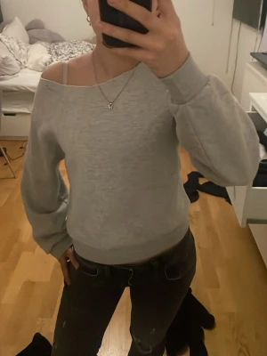 Ljusgrå offshoulder sweatshirt - Säljer en ljusgrå sweatshirt med offshoulder-design och långa ärmar. Tröjan har breda muddar vid ärmslut och midja, vilket ger en snygg och avslappnad look. Perfekt att matcha med jeans eller leggings för en chill stil.