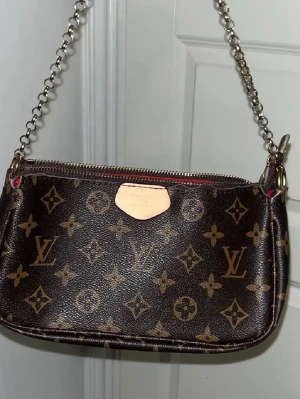 Monogram handväska - Säljer en snygg handväska. Väskan har en kedja som axelrem och dragkedja upptill. Perfekt storlek för det viktigaste och riktigt trendig design.