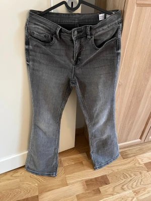 Grå bootcut jeans från Vero Moda, stl M/30 - Snygga grå jeans från Vero Moda med bootcut-snitt och klassisk femficksdesign. Jeansen har en mörkgrå tvätt med lätt slitning och är tillverkade i mjukt denim-material. 
