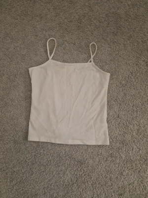 Vit linnetopp från Kappahl - Ett enkel och stilren vitt linne från Kappahl med tunna axelband. Linnet är rak i modellen och gjord i mjuk bomull, perfekt för varma dagar eller som lager under andra plagg.