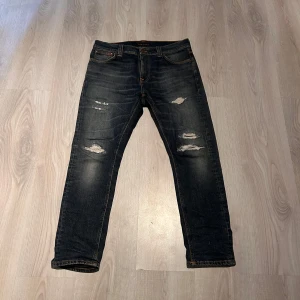 Nudie Jeans - Säljer ett par mörkblå jeans från Nudie Jeans med slitna detaljer. Jeansen har en straight passform och de är storlek W 30 L28. Jag är 176 väger 63kg o de sitter perfekt på mig så enligt mig så är storleken egentligen W 30 L 30. Hör av dig vid minsta fundering!