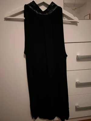 Svart ärmlös topp från Wera - Snygg svart ärmlös topp från Wera med dekorativa detaljer i silver runt halsen. Toppen har en lös passform och är tillverkad i ett mjukt, lätt material som ger ett elegant fall. Perfekt att styla med jeans eller kjol för en cool look. Öppen rygg