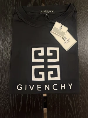 Svart oversized Givenchy t-shirt - Säljer en svart oversized t-shirt från Givenchy med stort vitt logotryck på bröstet. Tillverkad i 100% bomull för skön känsla och har klassisk rund hals och korta ärmar. Perfekt för dig som vill ha en clean och lyxig look.