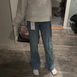 Ljusblå pleated flare jeans, strl 152 - Säljer ett par ljusblå pleated flare jeans i storlek 152. Byxorna har markerade sömmar längs benen och klassisk femficksdesign. Modellen är utsvängd nertill och har en snygg retrovibe. Perfekt för dig som gillar jeans med lite extra attityd.