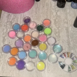 Nagelglitter och nagelstenar  - Säljer ett set med små burkar fyllda med nagelglitter och stenar i massor av färger, både matta och glittriga nyanser som blå, lila, orange, rosa, grön, gul och brun. Kommer i genomskinliga plastburkar som är enkla att ta med.