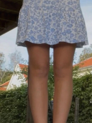 Blommig kortkjol i blått och vitt - Supersöt kortkjol med blått och vitt blommönster. Kjolen har en volangig nederdel och resår i midjan för skön passform. Perfekt för sommarn eller semestern! 💕Jag vet inte storleken men skulle gissa på S! 