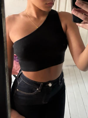 Svart oneshoulder topp - Säljer en svart ribbad oneshoulder topp från Even&Odd. Toppen är croppad och har en tight passform. Materialet är mjukt och stretchigt, vilket gör den riktigt bekväm🩷
