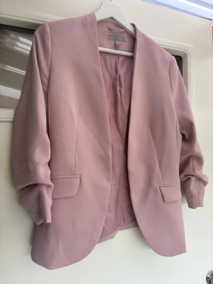 Ljusrosa kavaj 🎀 - Snygg ljusrosa kavaj från H&M med klassisk passform och långa ärmar. Kavajen har två fickor framtill och är helfodrad. Perfekt för dig som vill ha en stilren och fräsch look. Passar till många olika outfits och ger en soft vibe.💖