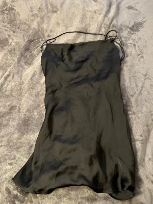 Svart satin klänning med tunna band - Säljer en svart kortklänning i satin med tunna axelband. Klänningen har en enkel och stilren design med lätt glansigt material som ger en lyxig känsla. Perfekt för dig som gillar minimalistisk stil och vill ha något som känns både trendigt och klassiskt.