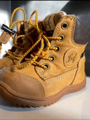 Bruna kängor från Leaf med snörning - Säljer ett par snygga kängor från Leaf i brunt skinn med mörkbrunt parti vid hälen. Skorna har gulbruna snören, grov sula och är vattentäta enligt ITC Waterproof-märkning. Perfekta för höst och vinter, med rund tå och robust design.