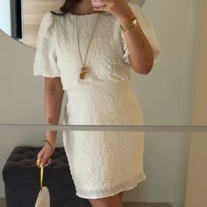 Vit kort klänning med rosett i ryggen - Superfin vit kort klänning med puffärmar och struktur i tyget. Klänningen har en snygg öppen rygg med stor rosett och dragkedja bak. Perfekt för dig som vill sticka ut med en söt och trendig look för studenten🤍