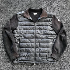 Moncler cardigan - Svart pufferjacka från Moncler med quiltad framsida och stickade ärmar samt rygg. Jackan har ribbad krage, två fickor med dragkedja och hel dragkedja framtill. Perfekt nu till hösten. Storlek M, passar någon som är runt 180 skulle jag säga. Skick 8/10 lite solblekt vid nacken men annars bra skick. Pris går att diskutera✅